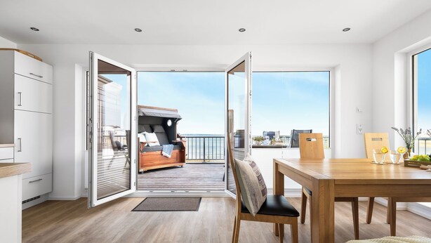 A modern interior with a wooden floor, a dining area with a table and chairs, and a balcony with a sofa and a view of the city.