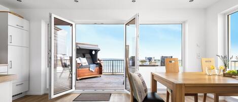 A modern interior with a wooden floor, a dining area with a table and chairs, and a balcony with a sofa and a view of the city.