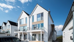 A modern two-story house with a balcony, a car parked in front, and a clear view of the sky. - Fjordblick– first row on the water, sauna, whirlpool, shower, fireplace, balcony (Olpenitz)
