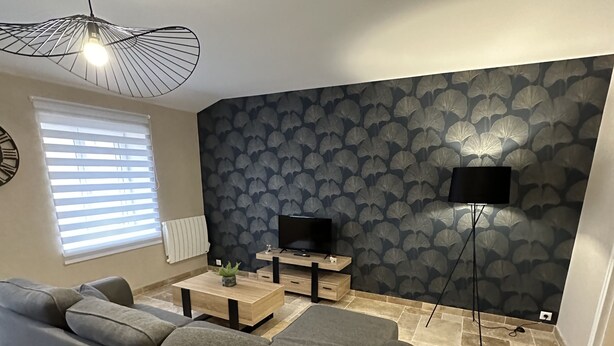 En moderne stue med en hjørnesofa, et sofabord, et fjernsyn på et stativ og tapet med mønster.