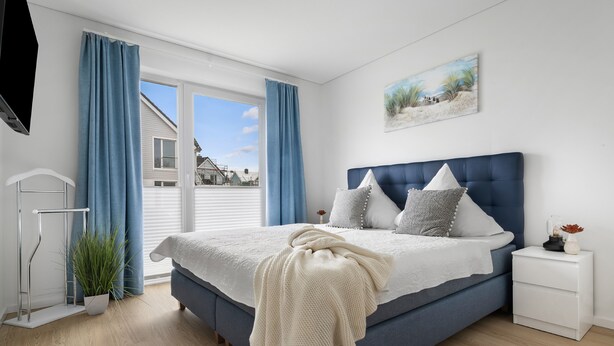 Ein Schlafzimmer mit einem großen Bett, einem Nachttisch, einer Pflanze und einem Bild an der Wand.