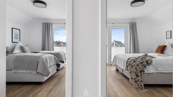 Una camera da letto moderna con un letto, un comodino, una finestra con tende e vista su una casa.