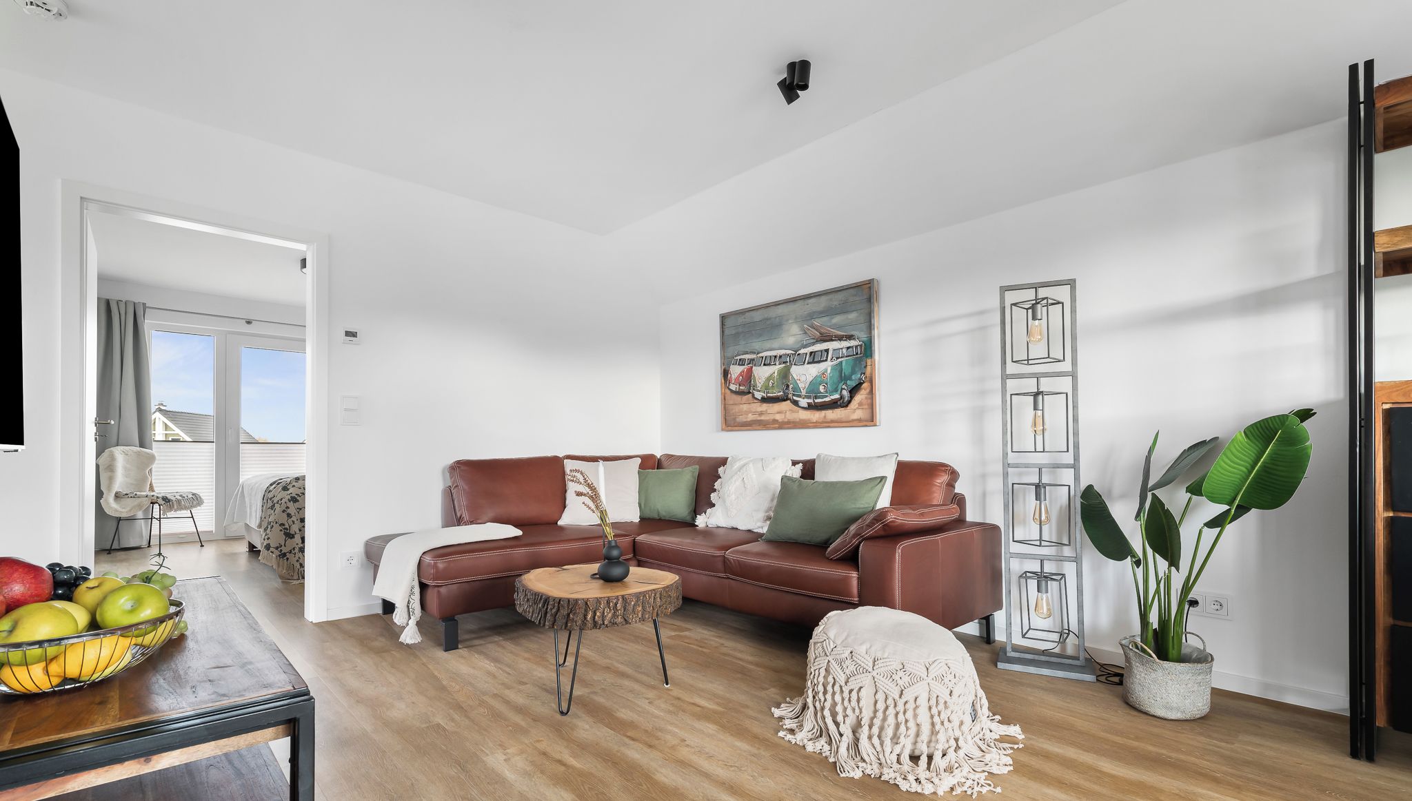 Ein modernes Wohnzimmer mit einem braunen Ledersofa, einem runden Couchtisch und einem Gemälde mit Oldtimern an der Wand.