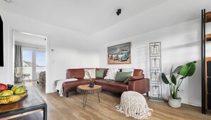A modern living room with a brown leather sofa, a round coffee table, and a painting of vintage cars on the wall.