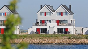 Ett tvåvåningshus vid vattnet med en balkong, ett garage och en liten uteplats.