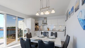 Ett modernt kök med vita skåp, en ugn i rostfritt stål och en matplats med ett bord som är dukat för fyra personer.