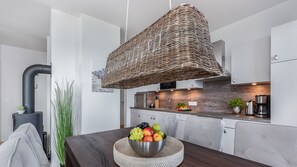 A modern kitchen with a central island, a hanging wicker light fixture, and a visible stove.