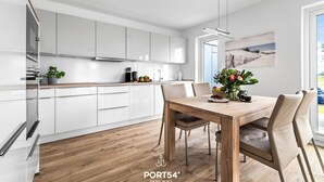 Une cuisine moderne avec des meubles blancs, une table à manger en bois et une vue sur l’extérieur.