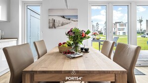 Un espace repas moderne avec une table en bois, des chaises en cuir, un vase rempli de fleurs et une vue sur la mer grâce à de grandes fenêtres.