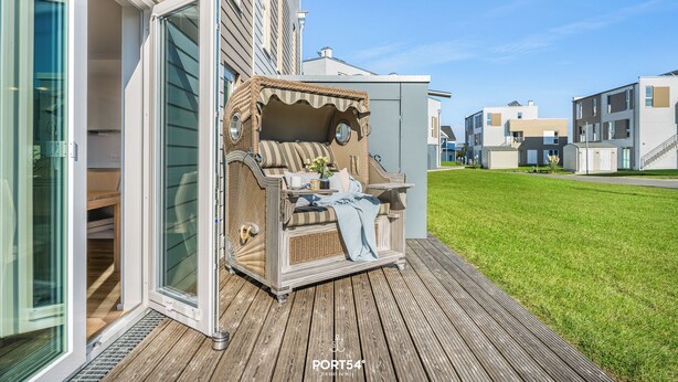 Une terrasse dotée d’un canapé en osier, d’une petite table avec un vase et d’une porte vitrée donnant sur une pièce.
