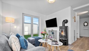 Una sala moderna con un sofá gris, un televisor de pantalla plana, una chimenea y una mesita con un jarrón de flores.