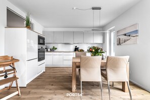 Moderni keittiö, jossa on valkoiset kaapit, puinen ruokapöytä ja kaksi tuolia.