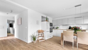 Una cocina moderna con armarios blancos, una mesa de comedor de madera y un taburete pequeño.