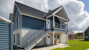 Uma casa moderna de dois andares com varanda, escada e gramado bem cuidado.