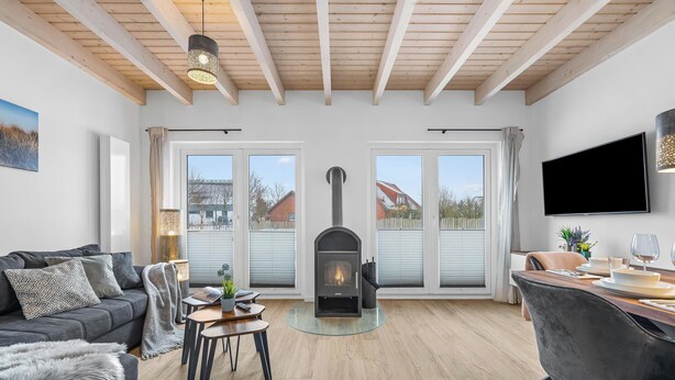 A living room with a fireplace, a sofa, a dining table with chairs, and a television mounted on the wall. - Ferienhaus Wattwächter Büsum (Büsum)