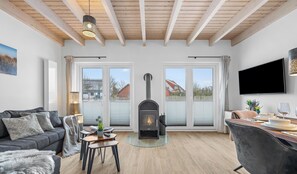 A living room with a fireplace, a sofa, a dining table with chairs, and a television mounted on the wall.
