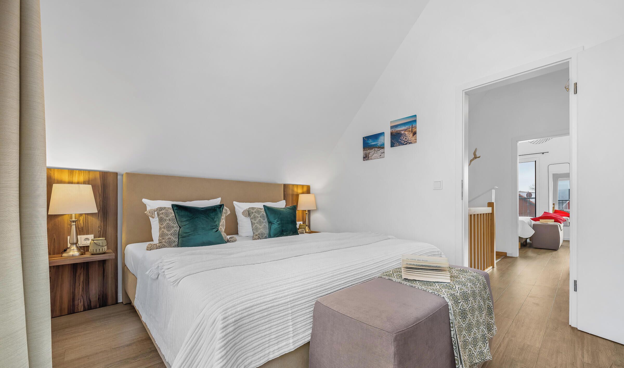 A bedroom with a bed, bedside tables, a nightstand, a window, and a door leading to another room.