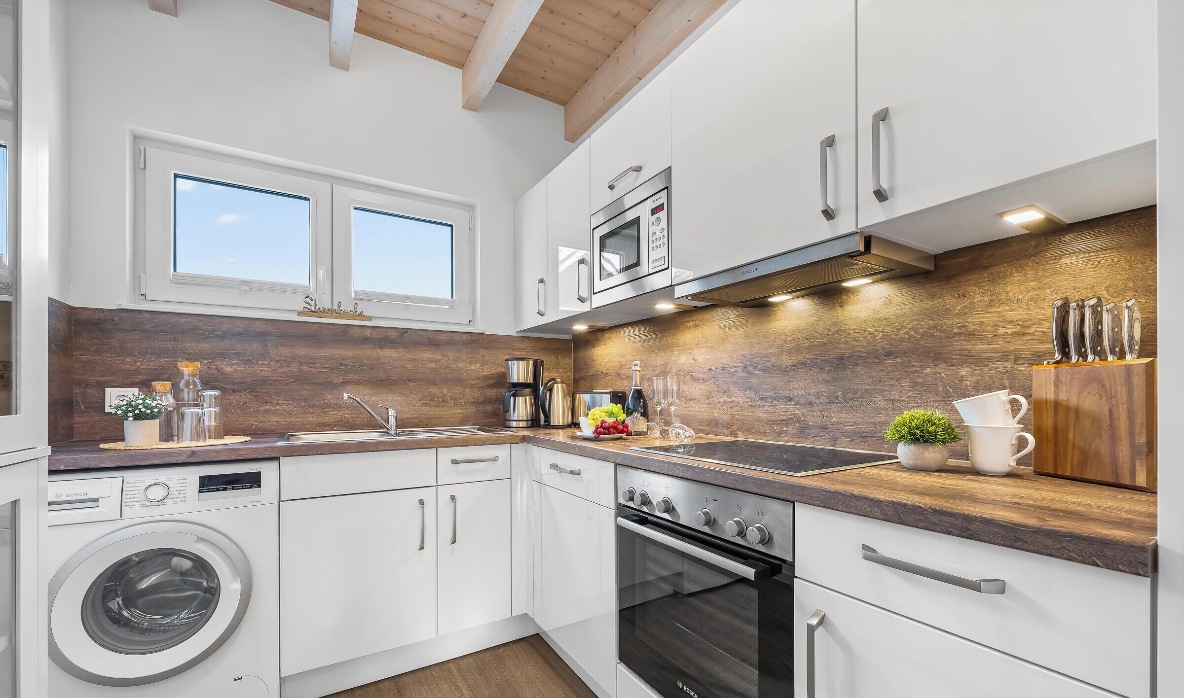 Cocina moderna con armarios blancos, lavadora Bosch, horno Bosch y encimera de madera.