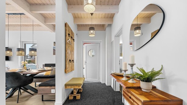 Un interior moderno con comedor, vigas de madera, un espejo y una planta.