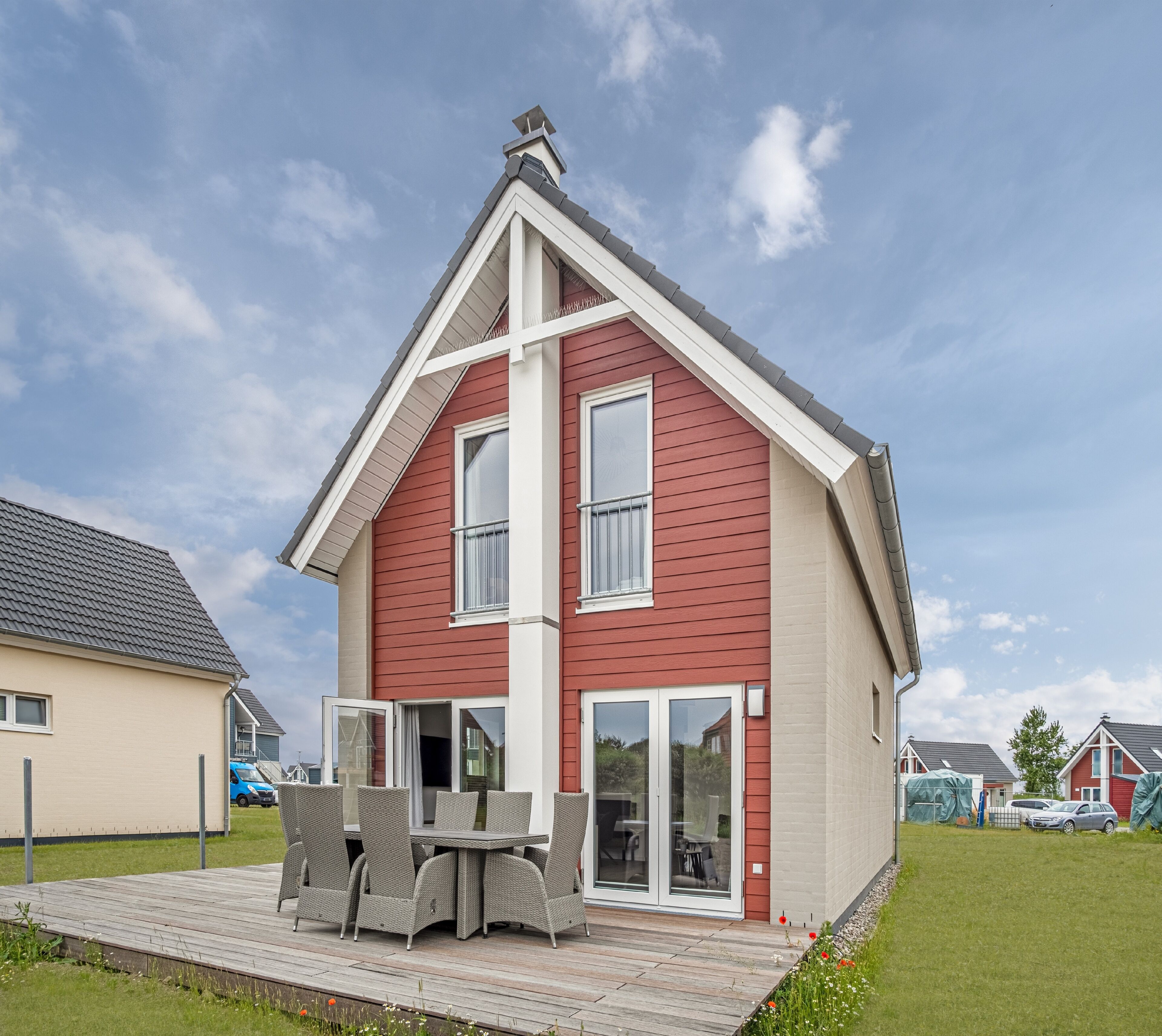 Une maison à deux étages avec une façade rouge, des boiseries blanches et un patio couvert aménagé avec du mobilier d’extérieur.