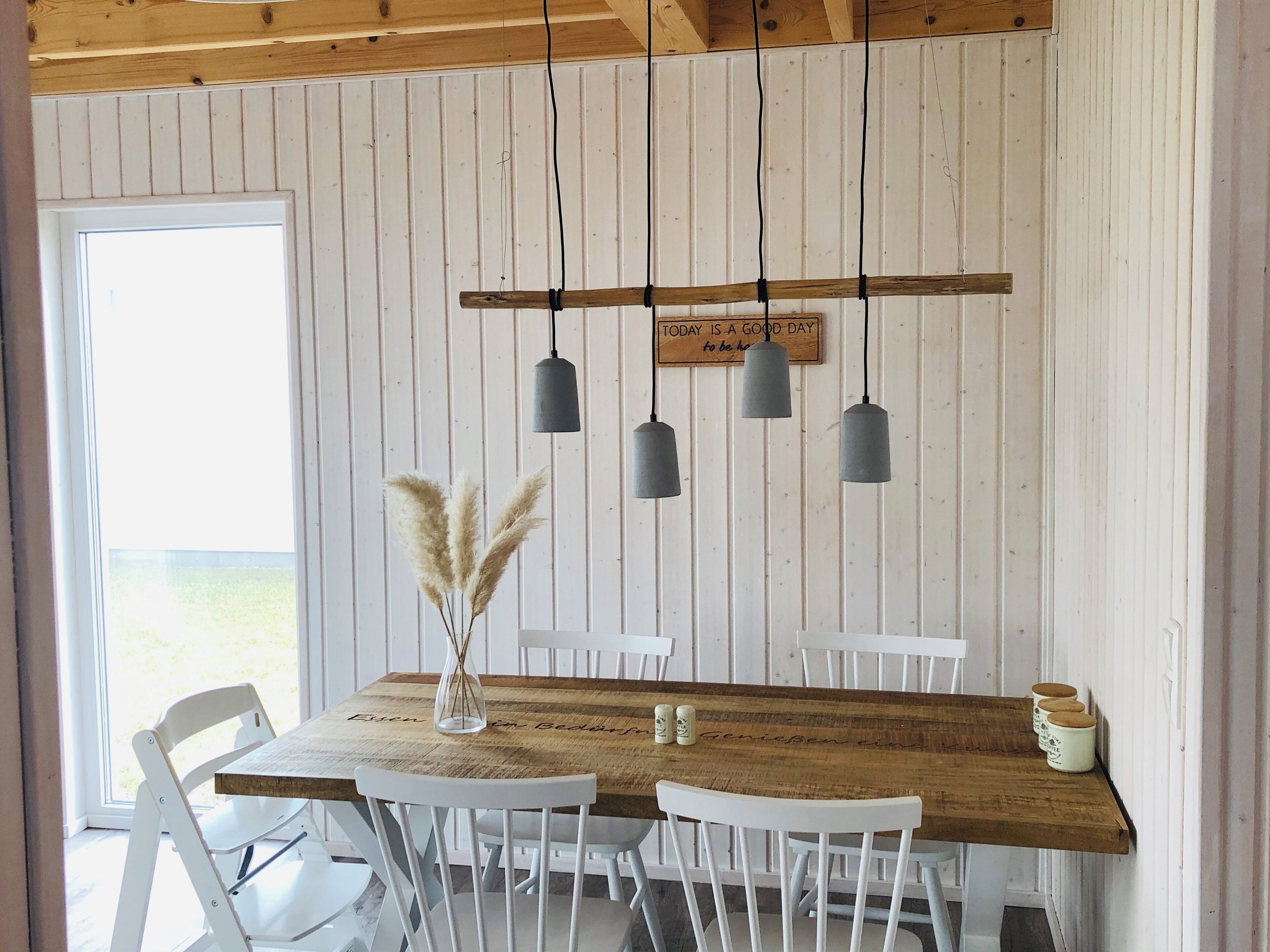 A dining area with a wooden table, white chairs, hanging pendant lights, and a decorative sign.