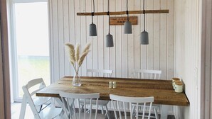A dining area with a wooden table, white chairs, hanging pendant lights, and a decorative sign. - Meerhaus - Detached House, Infrared Sauna, Fireplace, Bathtub, Terrace (Olpenitz)