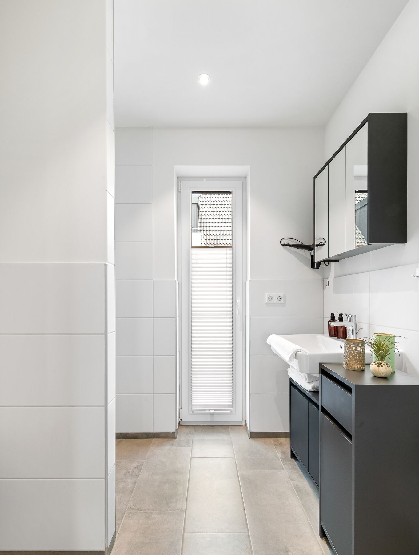 A modern bathroom with a white sink, dark cabinets, and a large mirror.