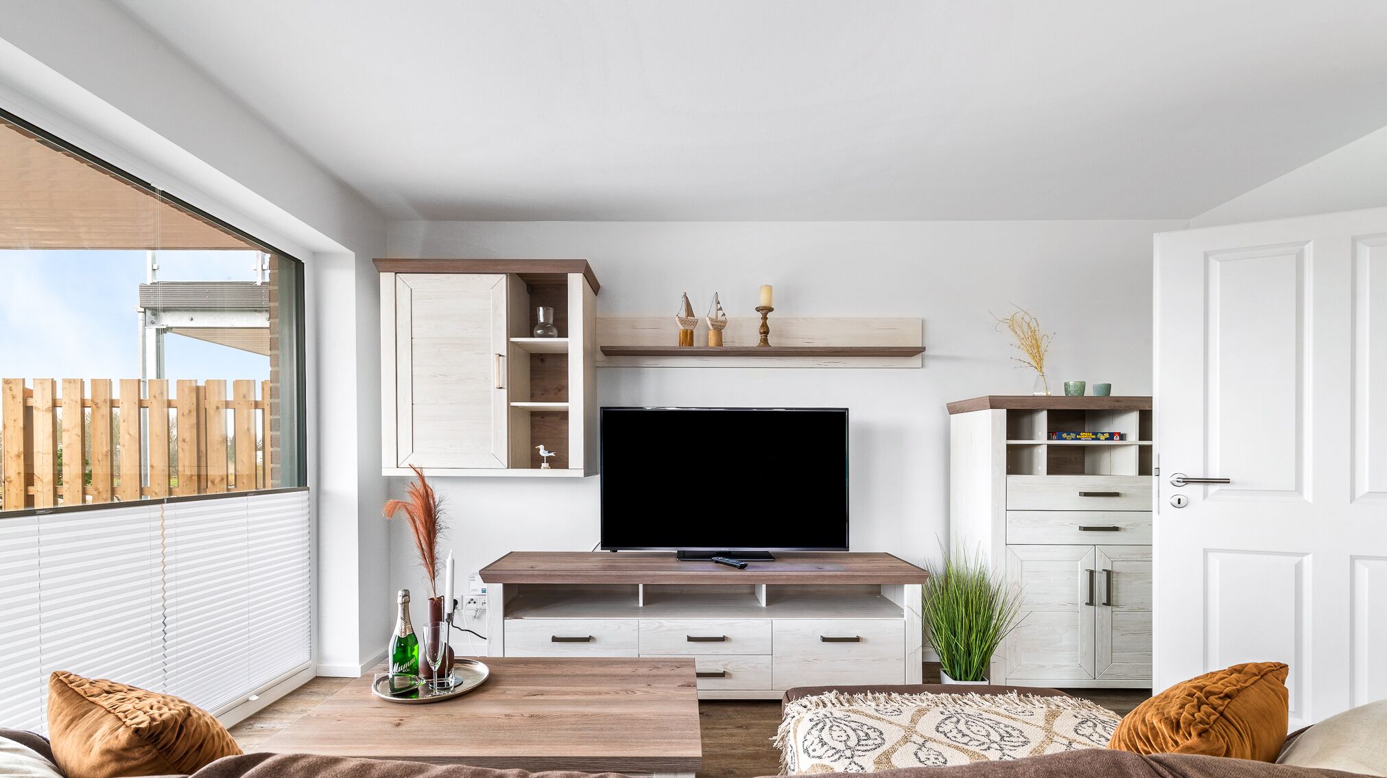 A modern living room with a TV, wooden cabinets, and a large window.