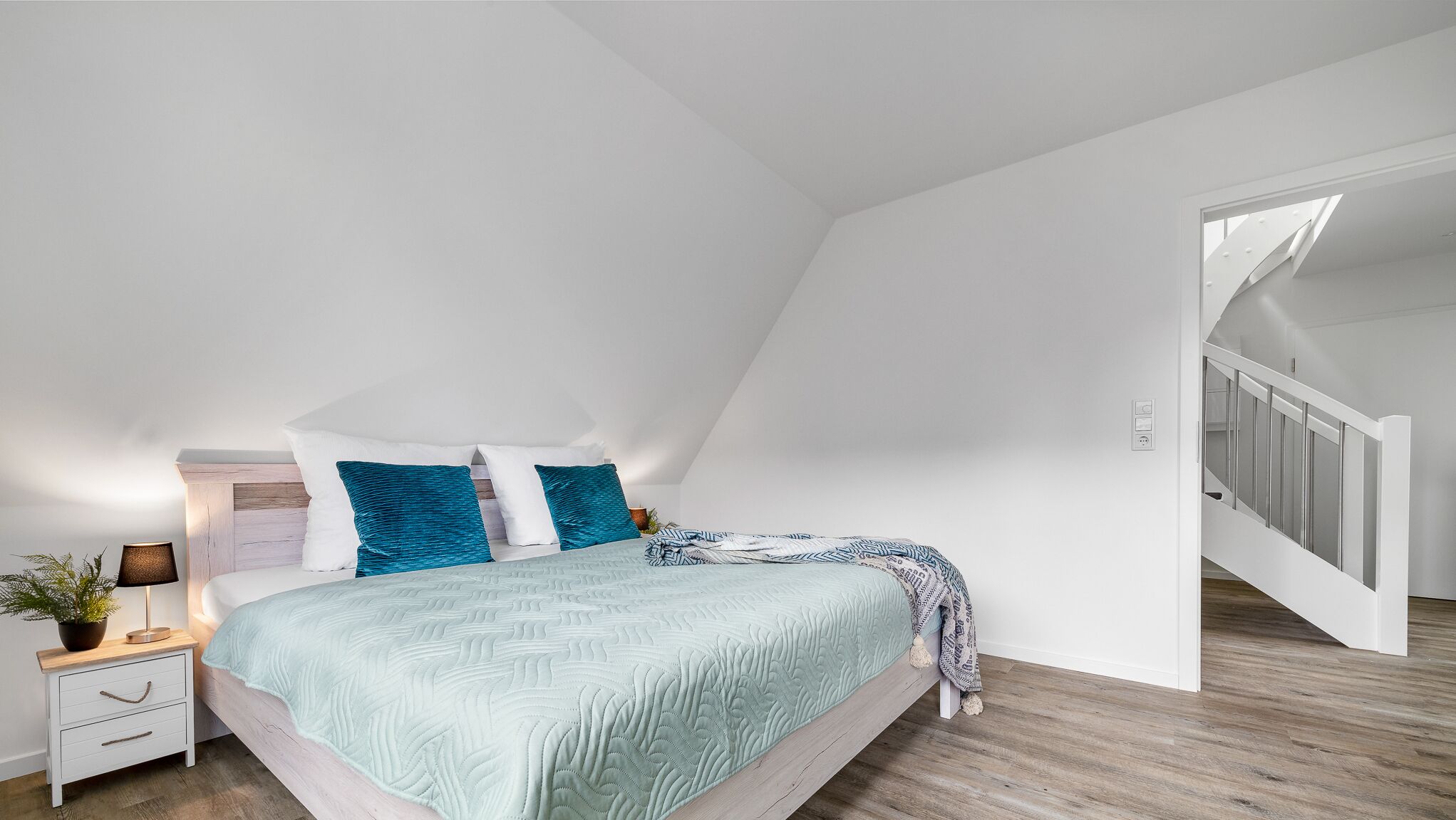 A bedroom with a bed, a nightstand, a lamp, and a potted plant.