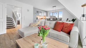 Un salon moderne avec un canapé gris, une table basse en bois et un vase de tulipes. Un escalier mène à l’étage supérieur.