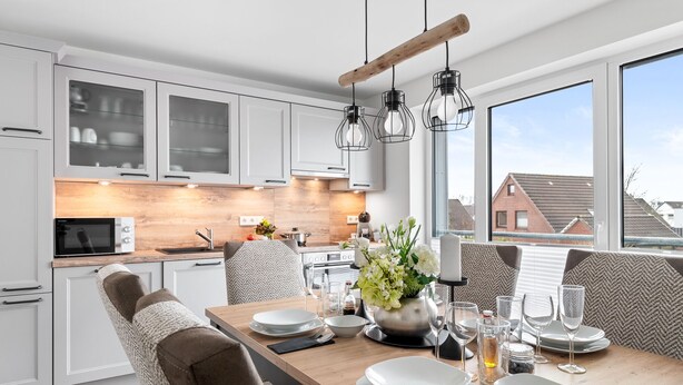 Une cuisine moderne avec des meubles blancs, un plan de travail en bois et un coin repas avec une table dressée pour deux personnes.