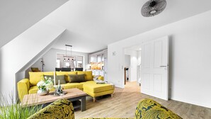 A modern living room with a yellow sofa, patterned armchairs, and a wooden coffee table. - Coast 8 - 2 bedrooms, shower room, balcony, stylishly furnished (Westerdeichstrich)