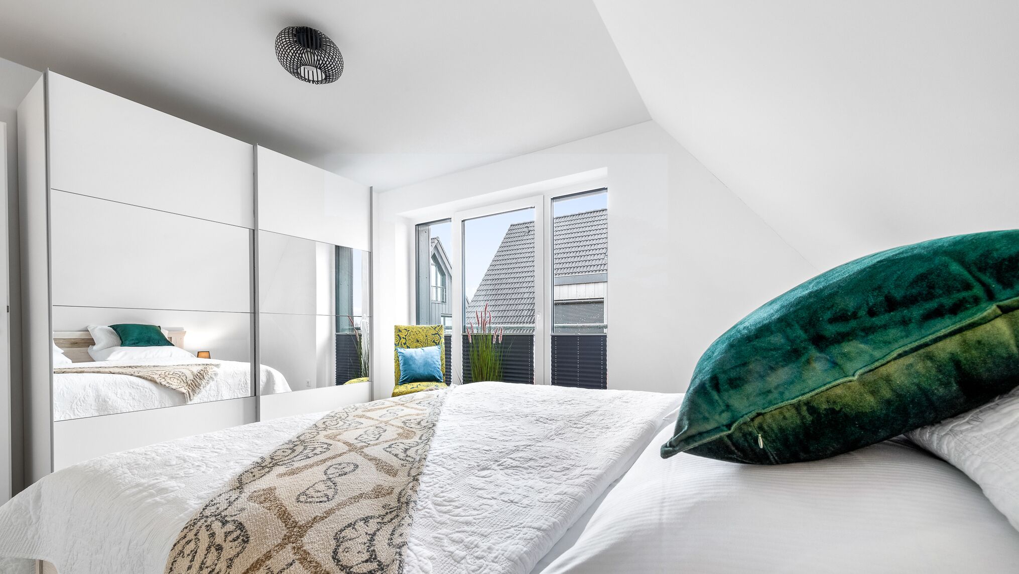 A modern bedroom with a large bed, a mirror, and a view of the outside.