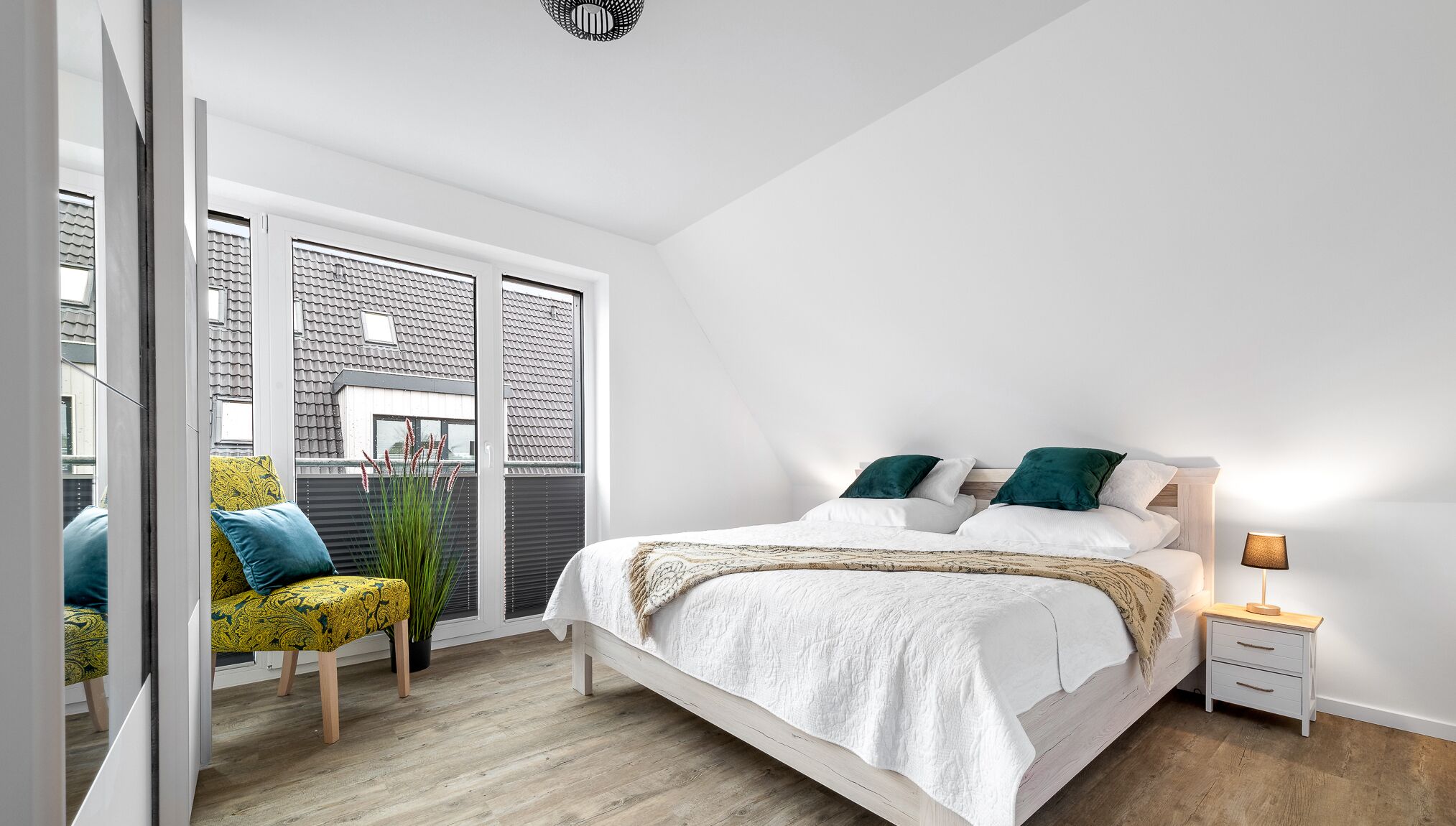 Ein Schlafzimmer mit einem großen Bett, Nachttischen, einem Sessel und Blick ins Freie.