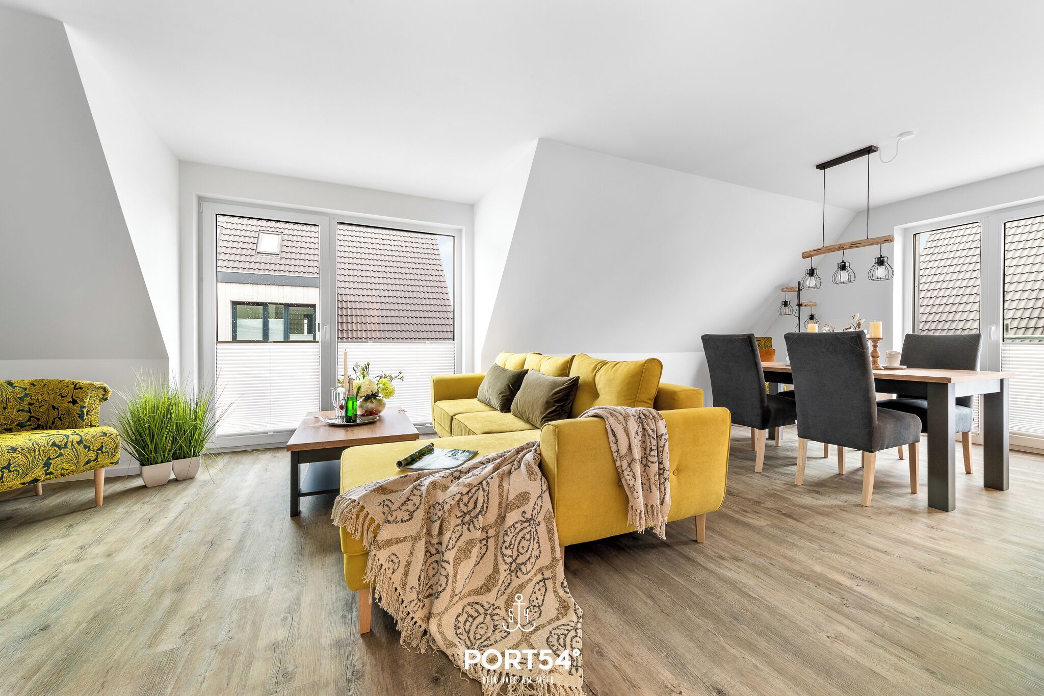 Un salon moderne avec un canapé jaune, une table à manger avec des chaises et une grande fenêtre équipée de stores.