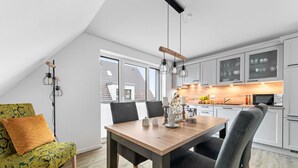 A modern kitchen with white cabinets, a wooden dining table, and a view of the outside through large windows. - Coast 8 - 2 bedrooms, shower room, balcony, stylishly furnished (Westerdeichstrich)