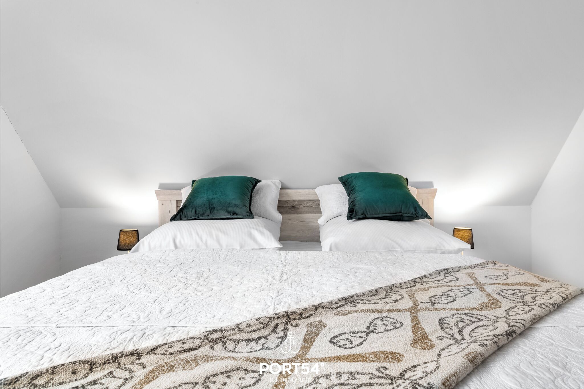 A bedroom with a bed, two pillows, a patterned throw, and bedside lamps.