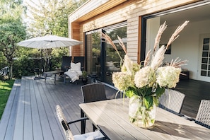 En træterrasse med udendørs møbler, blandt andet et bord og stole, samt en stor parasol.