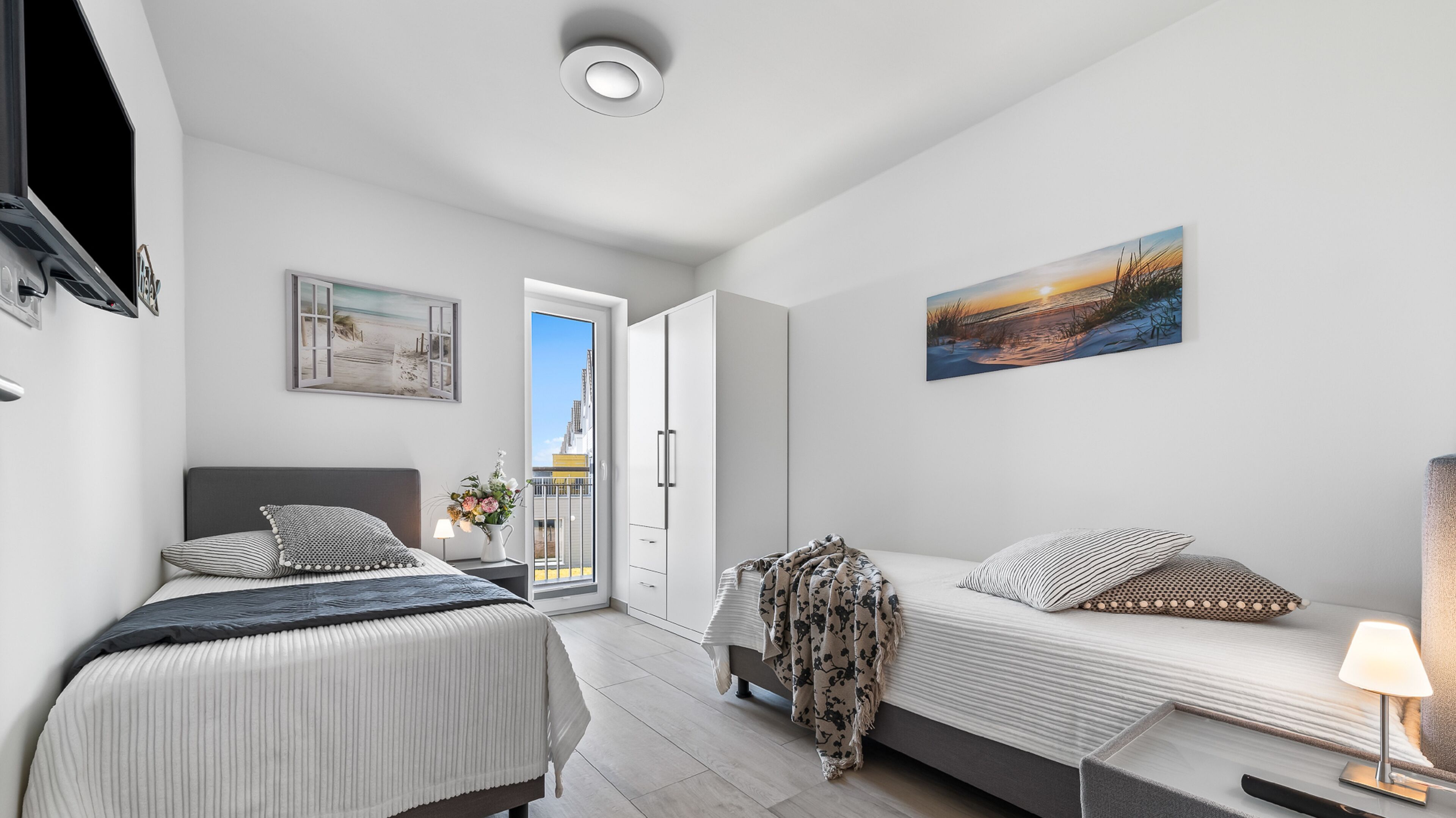 Une chambre moderne avec deux lits, une grande fenêtre et un tableau représentant un coucher de soleil.