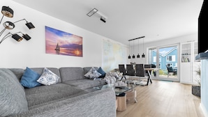 Ein modernes Wohnzimmer mit grauem Sofa, einem Glastisch und einem Essbereich mit Tisch und Stühlen.