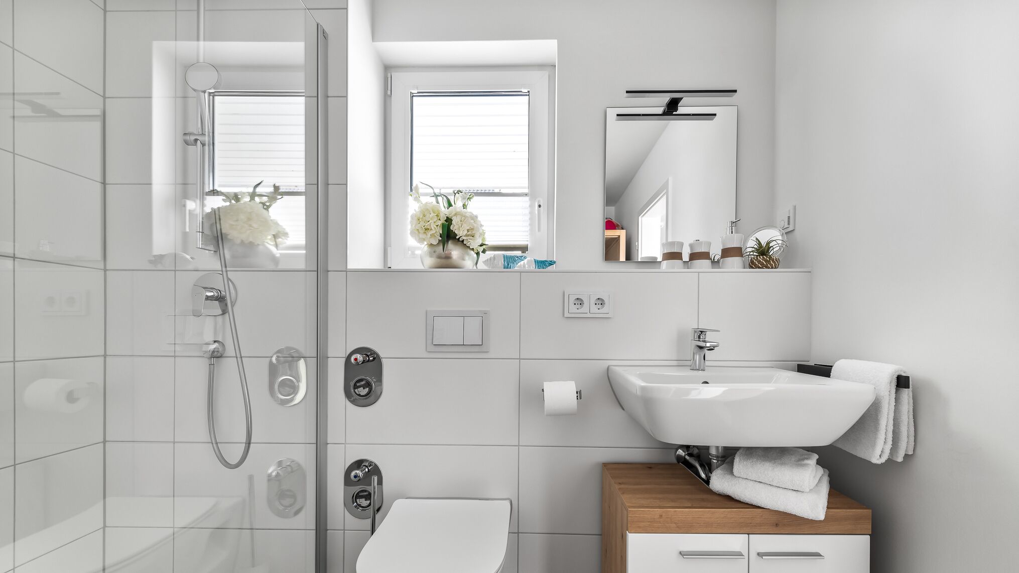 A modern bathroom with a glass-enclosed shower, a white sink, and a wooden vanity.
