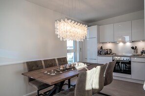Une cuisine moderne avec des meubles blancs, une table à manger en bois et un lustre original.