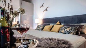 Un dormitorio con cama, almohadas, una botella de vino y una copa en una bandeja.