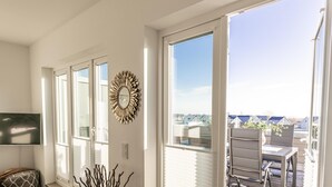 Una habitación luminosa con un ventanal grande, un televisor de pared y una zona de comedor con sillas y una mesa.