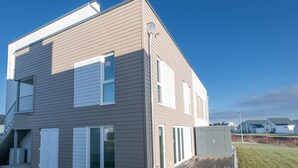 Una casa moderna de dos pisos con techo plano, un porche cubierto y una escalera visible que lleva al piso superior.