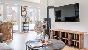 A modern living room with a large TV, a fireplace, and a dining area with a round table. - Diek No. 2 in the North Sea resort - close to the beach and the North Sea, fireplace, terrace, pets (Büsum)