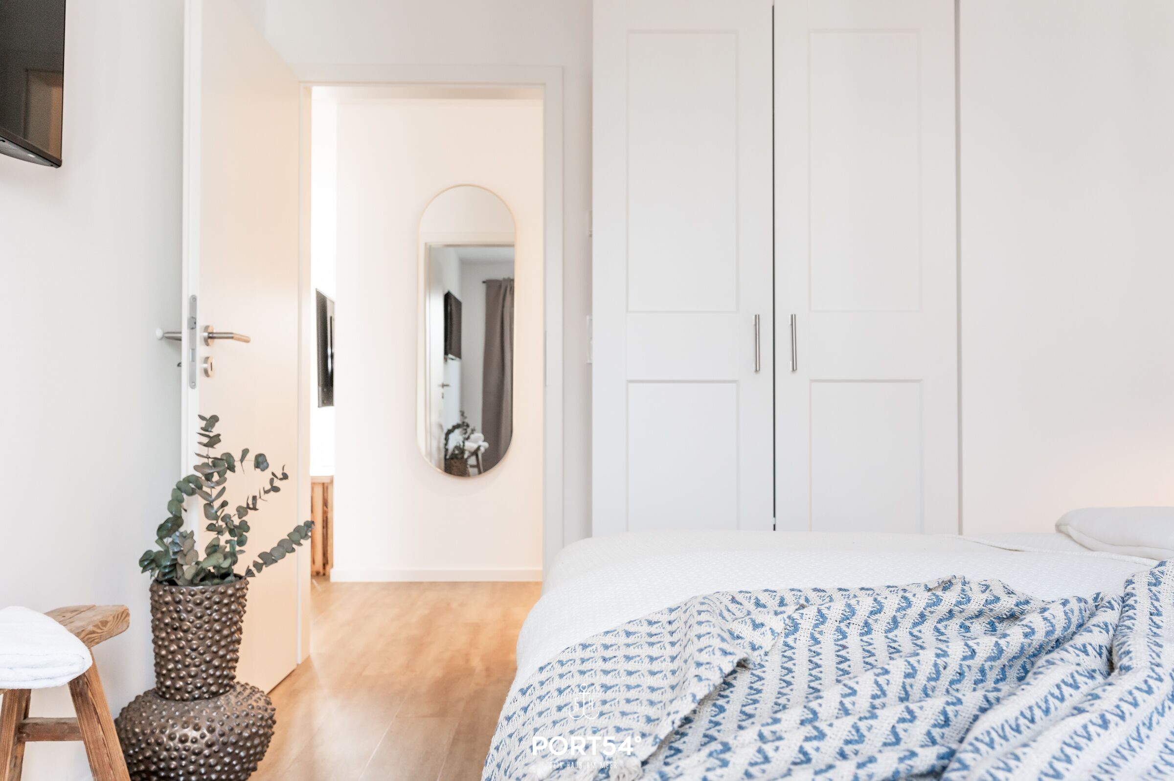 A bedroom with a bed, a wardrobe, a mirror, and a potted plant.
