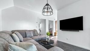 Un salon moderne avec un canapé d’angle, une table basse ronde et un téléviseur fixé au mur.