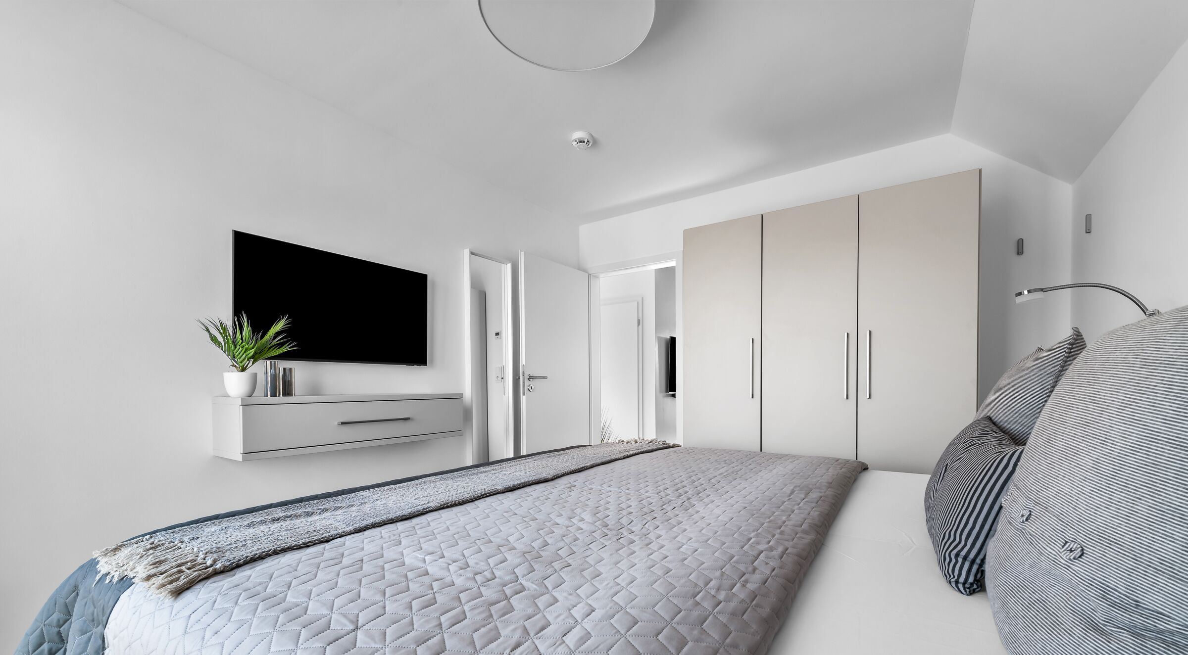 Een moderne slaapkamer met een groot bed, een aan de muur bevestigde televisie en een inloopkast met schuifdeuren.