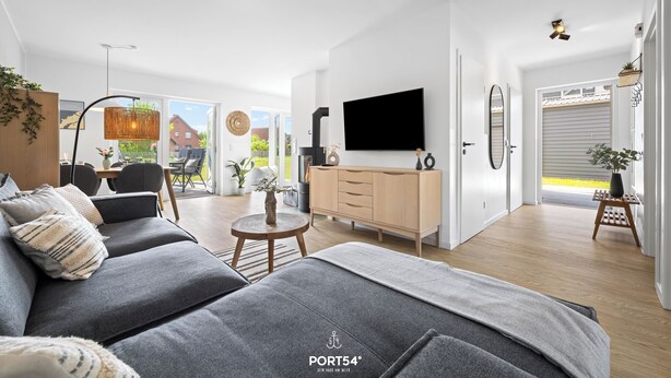 Ein modernes Wohnzimmer mit einem grauen Sofa, einem Fernseher, Holzböden und einem großen Fenster.